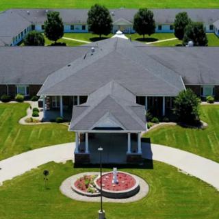 Aerial view of a large building surrounded by green lawns and trees, featuring a circular driveway and a fountain.