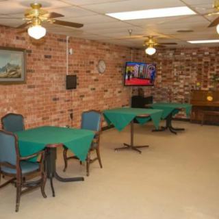 A dining area with tables and chairs against a brick wall, featuring a television and ceiling fans.
