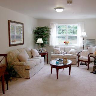 A cozy living room with sofas, chairs, and a coffee table, illuminated by natural light from a window.
