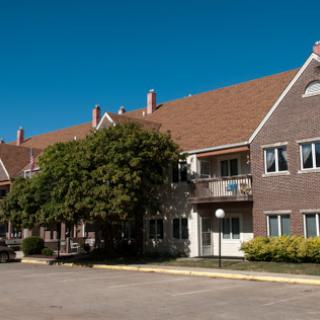 A modern apartment building featuring a brick exterior and well-maintained landscaping under a clear blue sky.