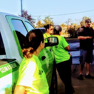 A group of workers in green shirts engages in conversation near a pickup truck during a sunny day.