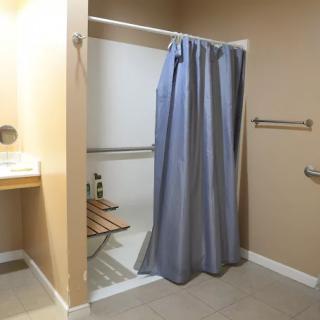 An accessible bathroom with a shower area fitted with a curtain and handrails.