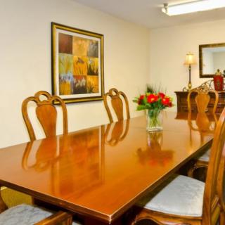A dining room with a wooden table, chairs, and a centerpiece flower vase.
