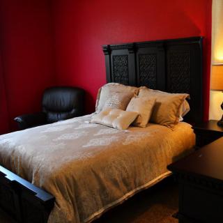 A cozy bedroom with a bed against a red wall, complemented by an armchair and a lamp.