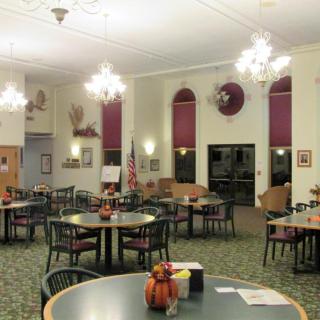 A well-lit dining area with tables and chairs arranged neatly, featuring chandeliers and decorative elements.