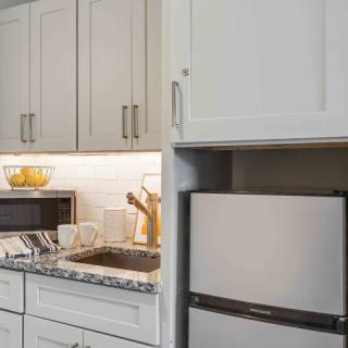 A modern kitchen with white cabinets, a small refrigerator, and various countertop appliances.
