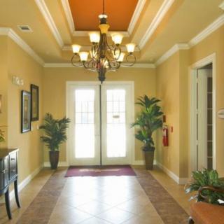 A warmly lit entryway with a chandelier, potted plants, and double French doors.