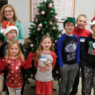 A cheerful group of children celebrating the holiday season in front of a decorated Christmas tree.