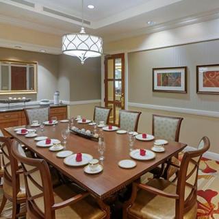 A well-appointed dining room with a large wooden table, set for a meal, surrounded by chairs and decorated with artwork and a chandelier.