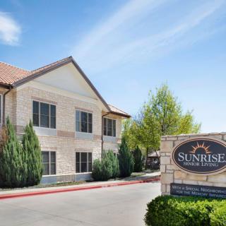 A two-story hotel building with a sign reading 'Sunrise Inn & Suites' set against a blue sky backdrop.