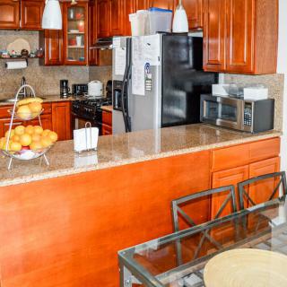 A modern kitchen with wooden cabinets, featuring a countertop with various appliances and seating.