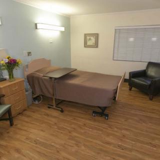 A clean and tidy hospital room with a bed, chairs, and flowers.