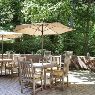 A serene outdoor patio with wooden tables and chairs under large umbrellas, surrounded by lush greenery.
