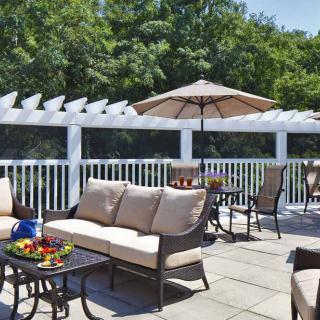 An inviting outdoor patio with comfortable seating and an umbrella, surrounded by lush greenery.