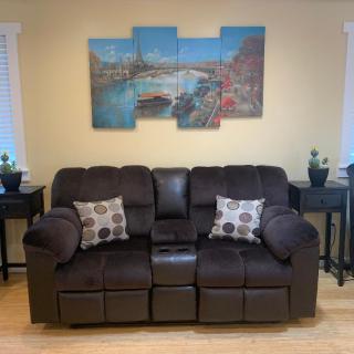 A cozy living room setup featuring a dark brown sofa with patterned pillows and a multi-panel artwork on the wall.