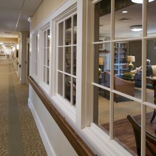 A well-lit interior hallway with large windows looking into a cozy room.