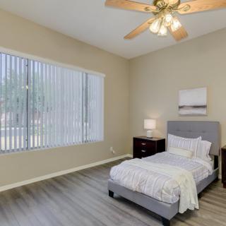 A minimalist bedroom with a single bed, nightstand, and a large window with blinds.