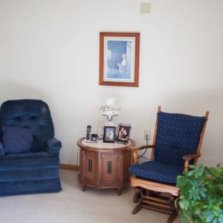 A cozy corner in a living room featuring a blue armchair, a matching blue rocking chair, and a wooden side table with decorative items.