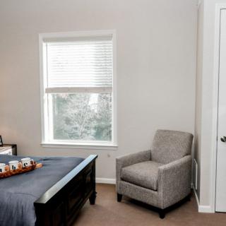 A minimalist bedroom featuring a gray armchair by a window.