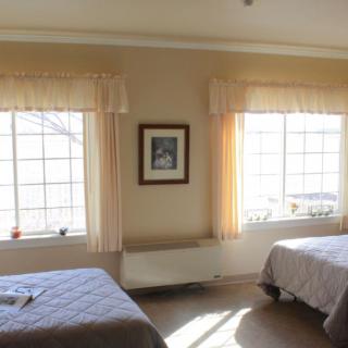 A bright bedroom with two beds and large windows letting in natural light.