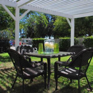 A cozy outdoor patio setup with a table and chairs under a pergola, featuring a refreshing pitcher of lemonade.