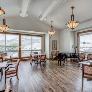 A spacious dining area with elegant chandeliers, a piano, and large windows offering natural light.