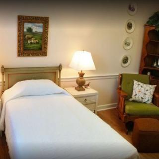 A cozy bedroom with a single bed, bedside lamp, and an armchair.