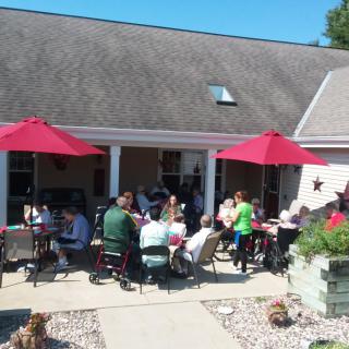 A group of people sitting together under red umbrellas on a sunny patio.