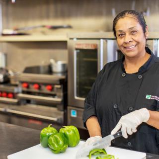 A chef smiling while cutting green peppers in a professional kitchen.
