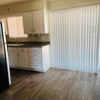 A modern apartment kitchen with wood flooring, white cabinets, and a refrigerator.