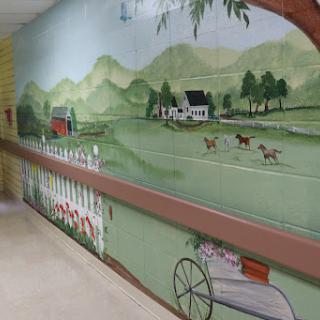 A vibrant mural depicting a serene countryside scene with rolling hills, a farmhouse, and grazing animals.
