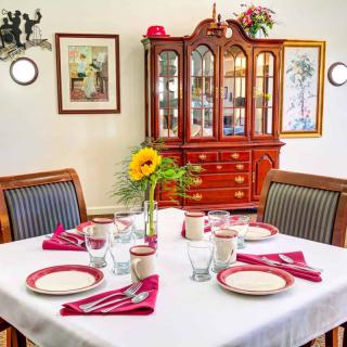 A well-set dining table with a flower centerpiece and a china cabinet in the background.