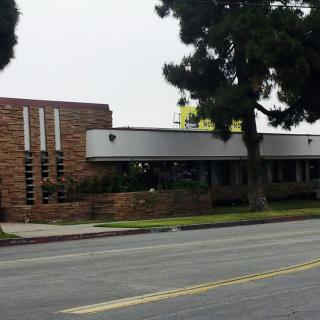 A commercial building on a quiet street with trees and an overcast sky.