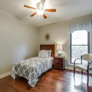 A cozy bedroom with a single bed, wooden flooring, and a ceiling fan.