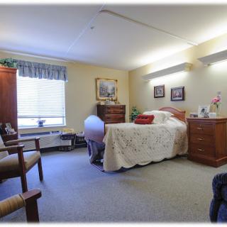 A cozy bedroom with a bed, dresser, and chairs near a window.
