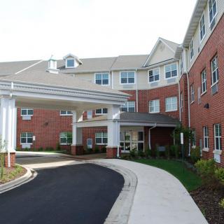 A view of a large residential building with a covered entrance and landscaped surroundings.