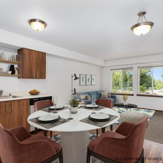A modern dining room with a round table set for four, featuring large windows and stylish decor.