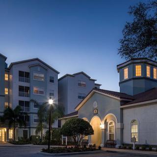 A serene evening view of a residential building complex with illuminated windows and surrounding trees.