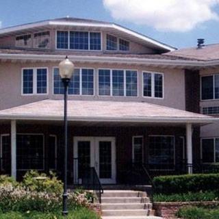 A two-story residential building with a porch, large windows, and a garden in front.