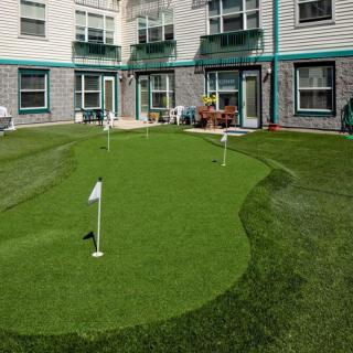 A small putting green set up in the backyard of a residential building with artificial turf and flags.