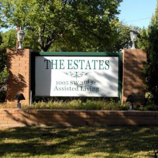 A sign for 'The Estates' assisted living facility displayed on a brick wall surrounded by trees.