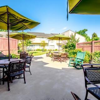 A sunny outdoor patio area with tables, chairs, and umbrellas.