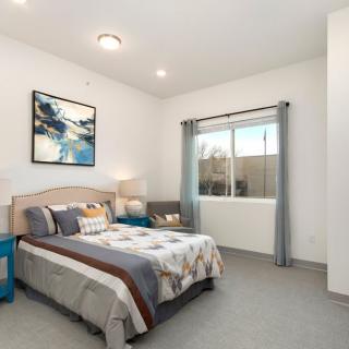 A modern bedroom interior with a bed, artwork, and natural light from a window.