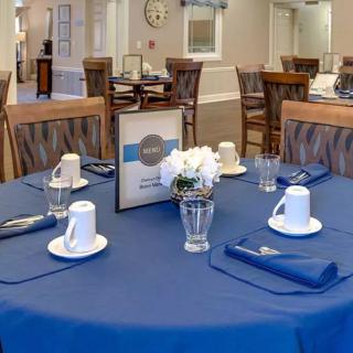 A neatly set dining table with a blue tablecloth and a small flower arrangement at the center.