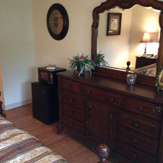 A cozy bedroom features a classic dresser with an ornate mirror, complemented by decorative plants and a lamp.