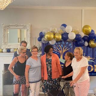 A group of people posing for a celebration with balloons and decorations in the background.