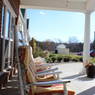 A row of rocking chairs on a sunny porch overlooking a garden.