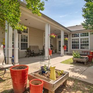 A cozy patio area with potted plants, benches, and hanging baskets under a clear blue sky.