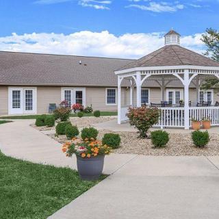 A charming outdoor area featuring a gazebo, surrounded by well-maintained gardens and pathways under a clear blue sky.
