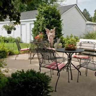 A serene outdoor patio area featuring metal furniture, potted plants, and a decorative statue surrounded by greenery.